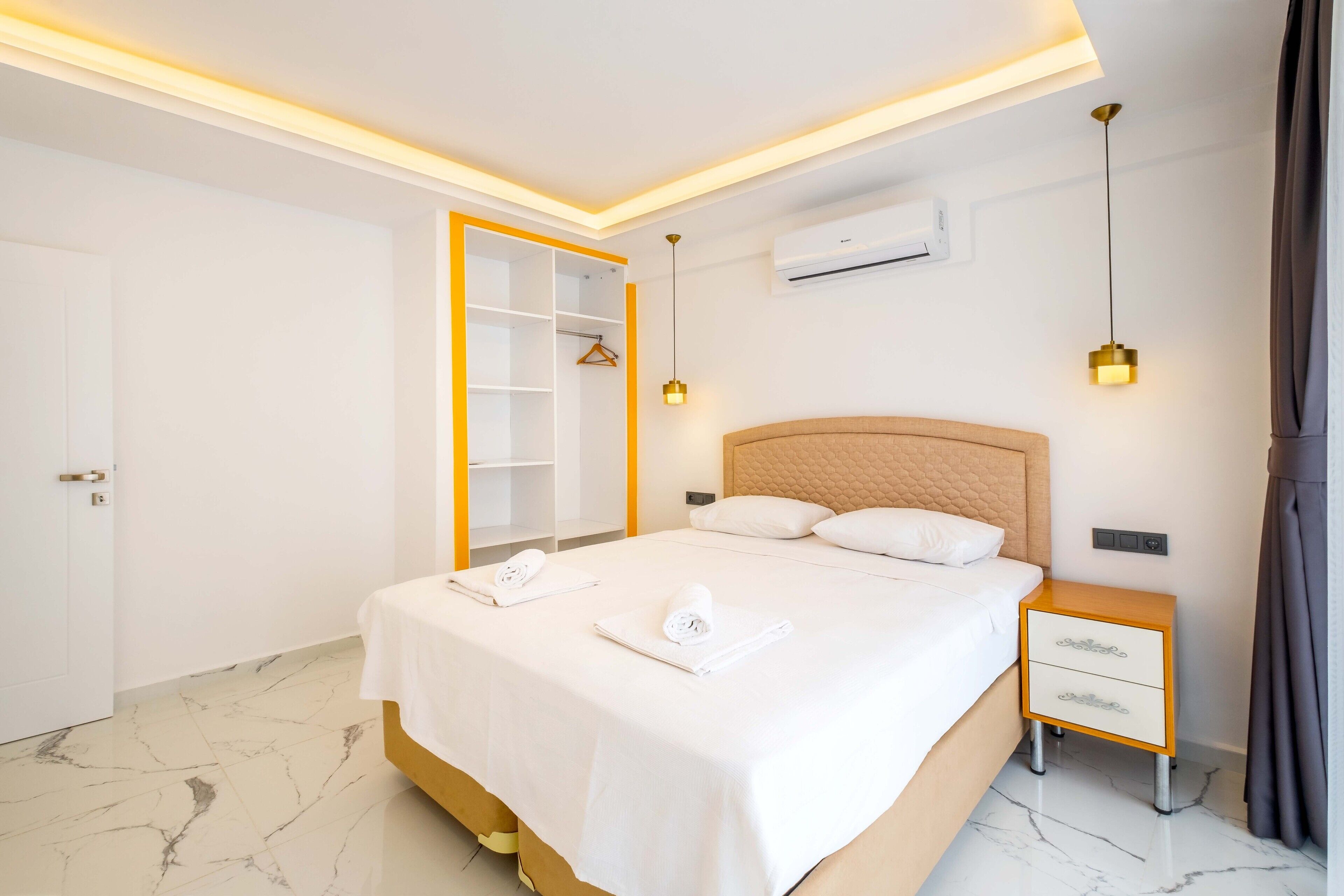 A hotel room with a bed, bedside table, wardrobe, and an air conditioning unit.