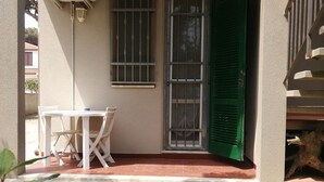 A covered outdoor seating area with a table and chairs, a green door, and a window with bars. - Beachfront (Lido di Spina)