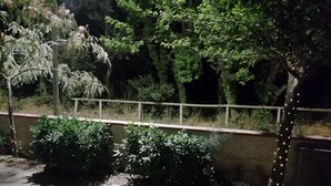 A nighttime outdoor area with a paved walkway, a metal railing, and various trees and shrubs. - Beachfront (Lido di Spina)