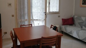 A dining area with a wooden table and chairs, a sofa with patterned cushions, and a window with curtains. - Beachfront (Lido di Spina)