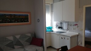 A compact living space with a kitchenette, a sofa with a patterned cover, and a painting on the wall. - Beachfront (Lido di Spina)