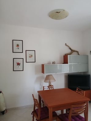 A dining area with a wooden table and chairs, a lamp, and framed floral artwork on the wall.