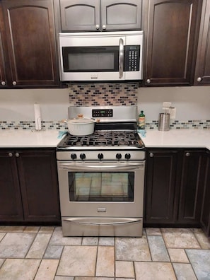 Una cocina con gabinetes de madera oscura, un microondas de acero inoxidable, una estufa a gas y un horno empotrado.
