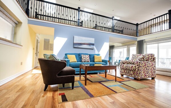 Amplia sala de estar con un sofá azul, un sillón estampado y una mesa de centro de madera. Una escalera conduce a un nivel superior.