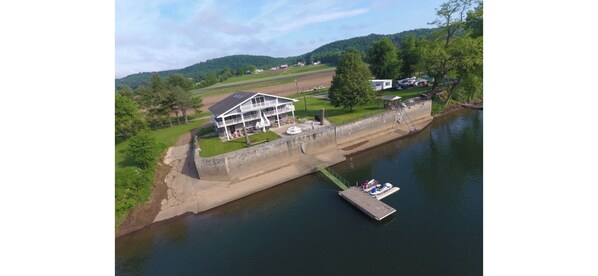 Una propiedad junto al río con muelle, una casa grande con balcón y un área verde.