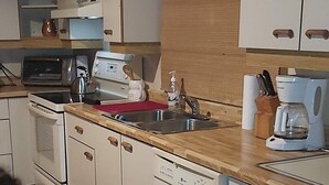 Une cuisine compacte avec des meubles blancs, un plan de travail en bois, un grille-pain, une bouilloire et une machine à café.