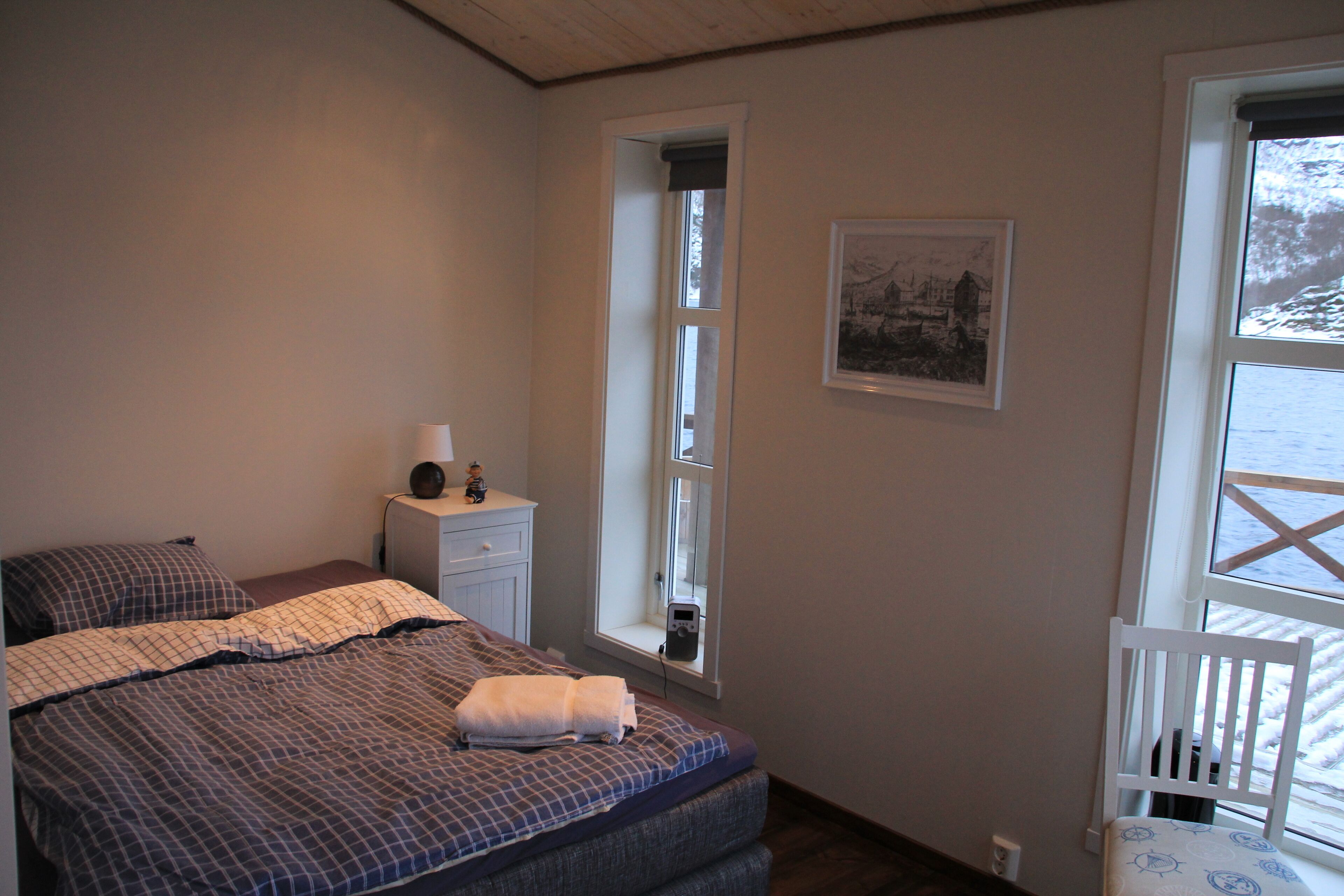 Een slaapkamer met een bed, een nachtkastje, een stoel en twee ramen.