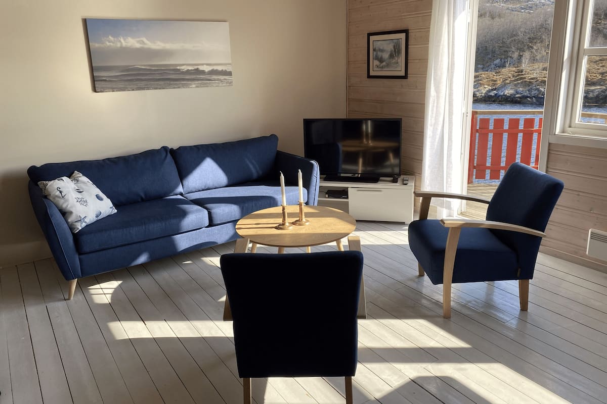 A living room with a blue sofa, a coffee table, and two chairs. There is a TV on a stand and a painting on the wall.