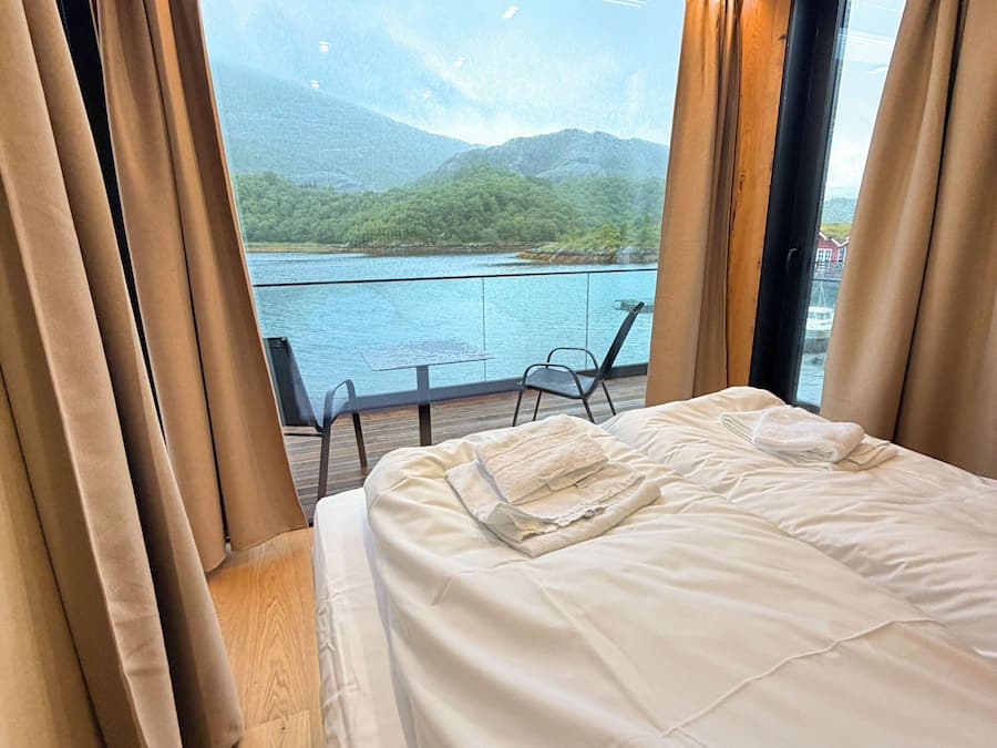 A bedroom with a large bed, a view of a lake, and a balcony with chairs.