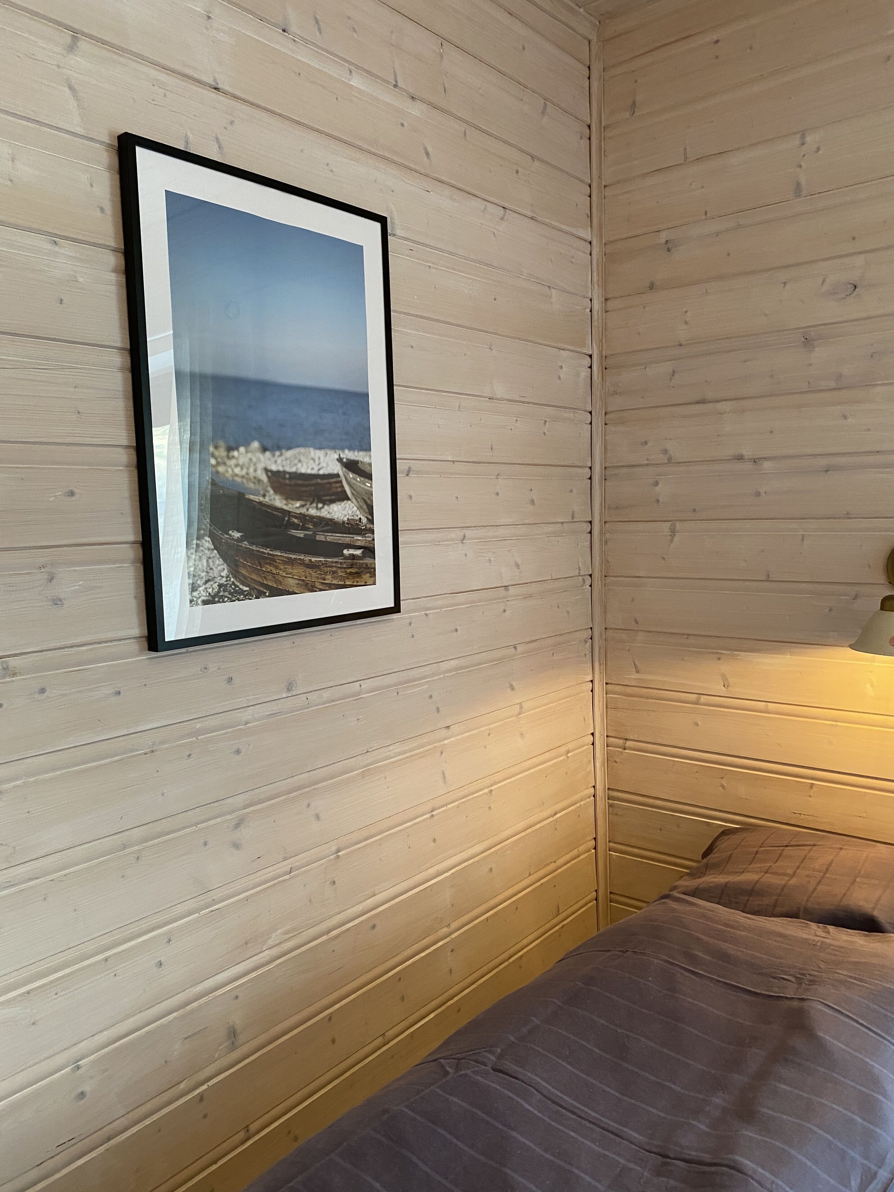 Ein Zimmer mit einer Holzwand, einem Bilderrahmen mit einer Strandansicht und einem Bett mit einer braunen Decke.