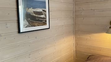Ein Zimmer mit einer Holzwand, einem Bilderrahmen mit einer Strandansicht und einem Bett mit einer braunen Decke.