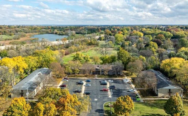 An aerial view of a parking lot with several cars, surrounded by trees and a building with a sloped roof.