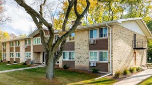 A multi-story apartment building with a brick facade, large windows, and a tree in the front yard. - Liberty Valley Studios in Madison, Wi! (Madison)