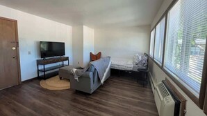 A compact room with a bed, a sofa, a TV, and a window with blinds. - Liberty Valley Studios in Madison, Wi! (Madison)