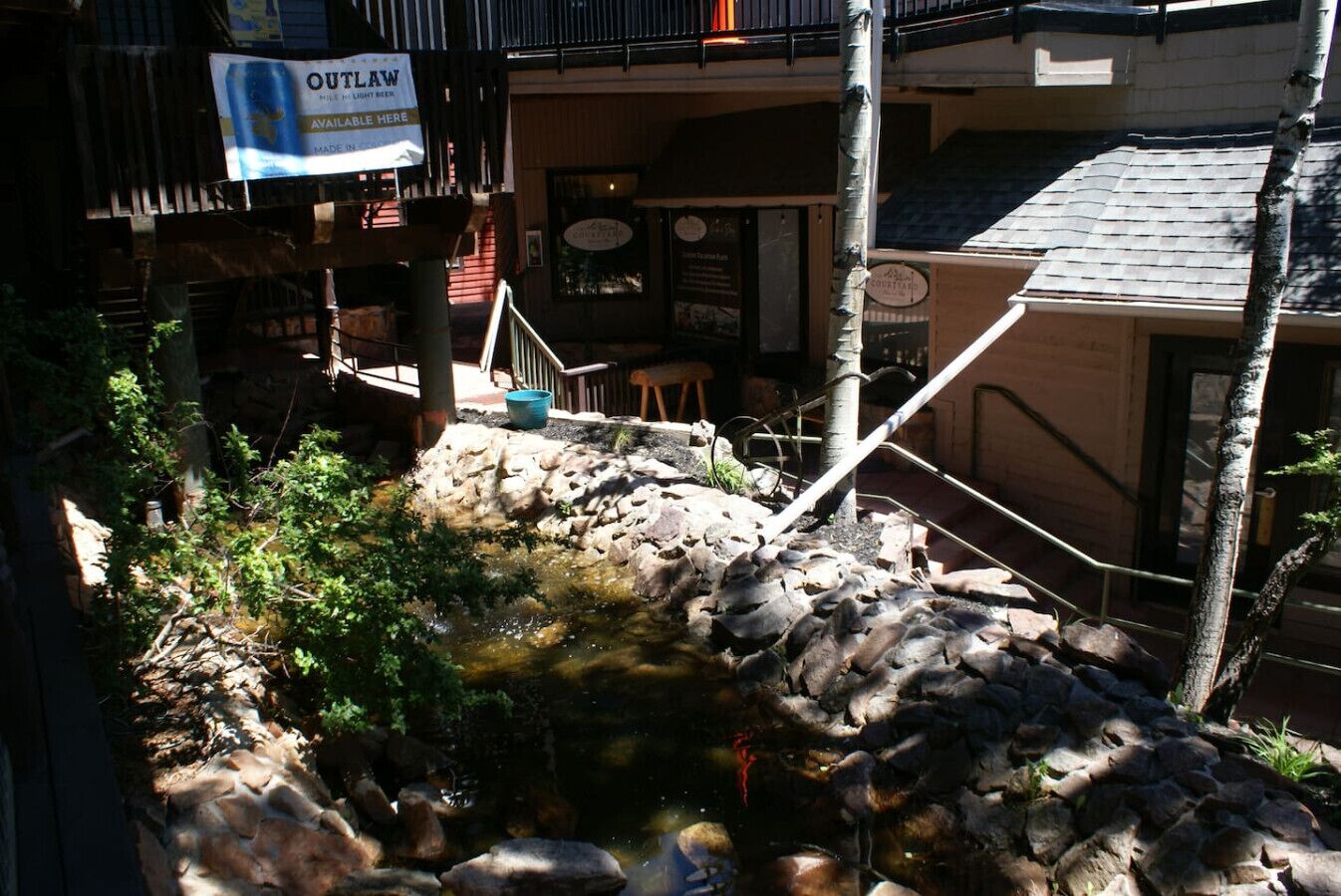 A small outdoor pond with rocks and plants, a wooden staircase, and a building with a sign that reads "OUTLAW".