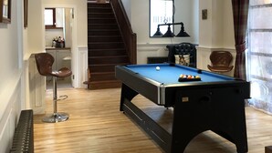 Een pooltafel in een ruimte met houten vloeren, een trap en een eethoek.