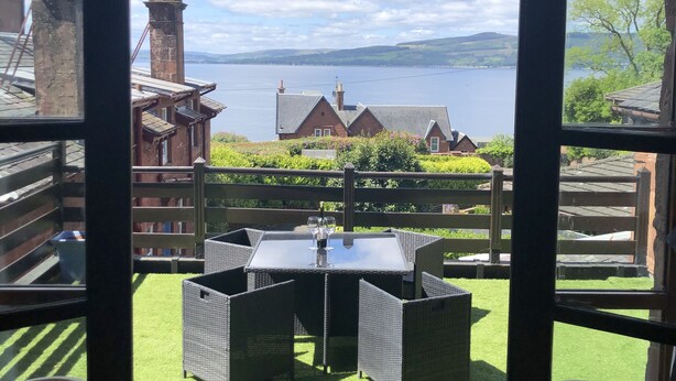 Uitzicht vanuit een gebouw op een terras met een tafel en stoelen, een gazon en een waterpartij op de achtergrond.