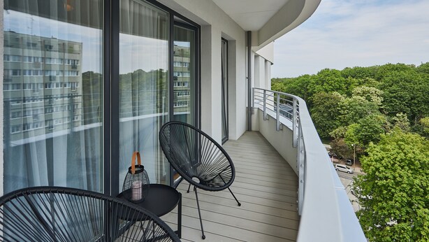 En balkon med to sorte stole, et lille bord og en flaske.