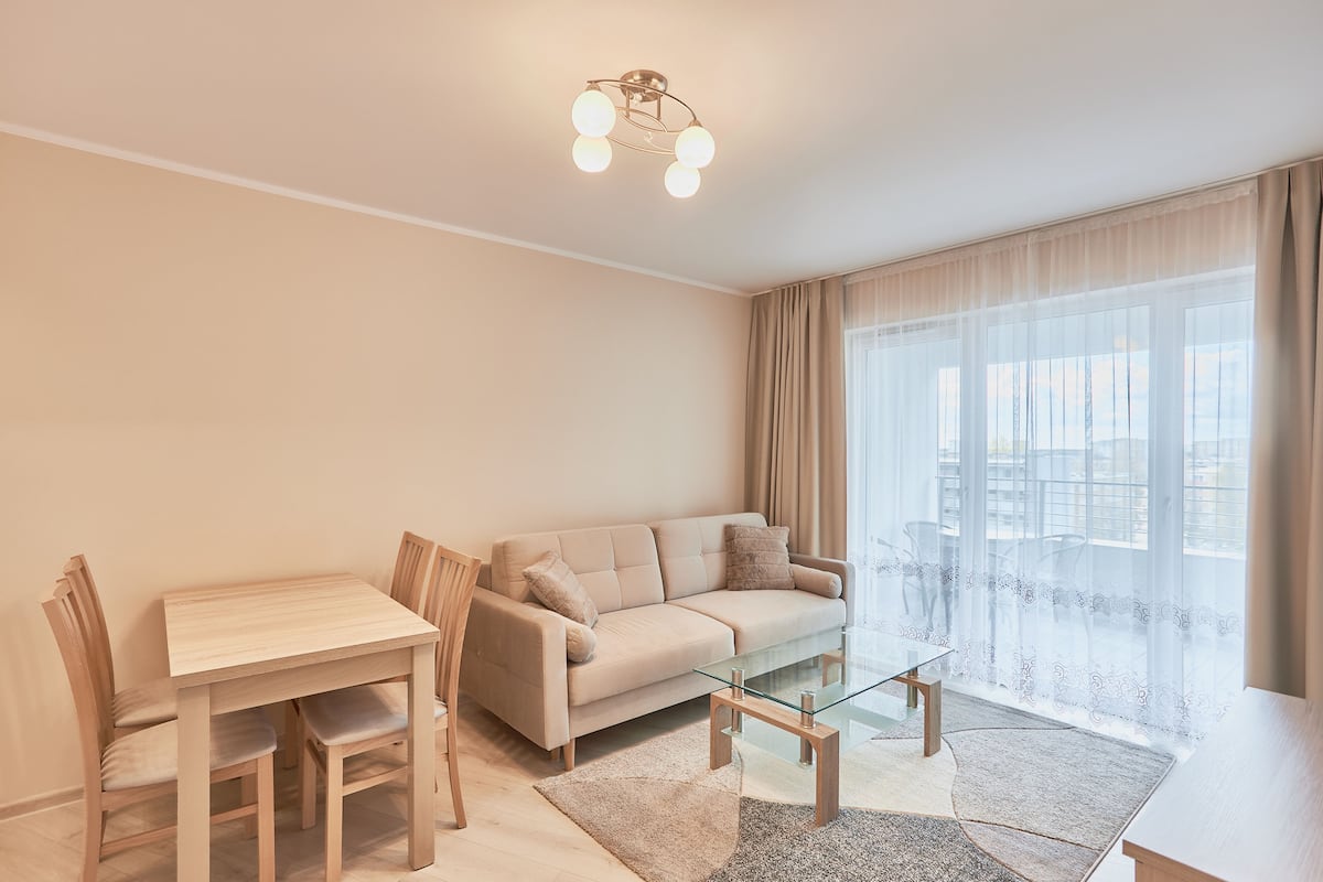 A modern living room with a sofa, a glass coffee table, and a dining table with chairs.
