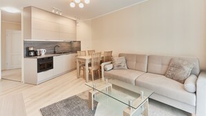 En moderne stue med et glasbord, en beige sofa og et spiseområde med træstole.