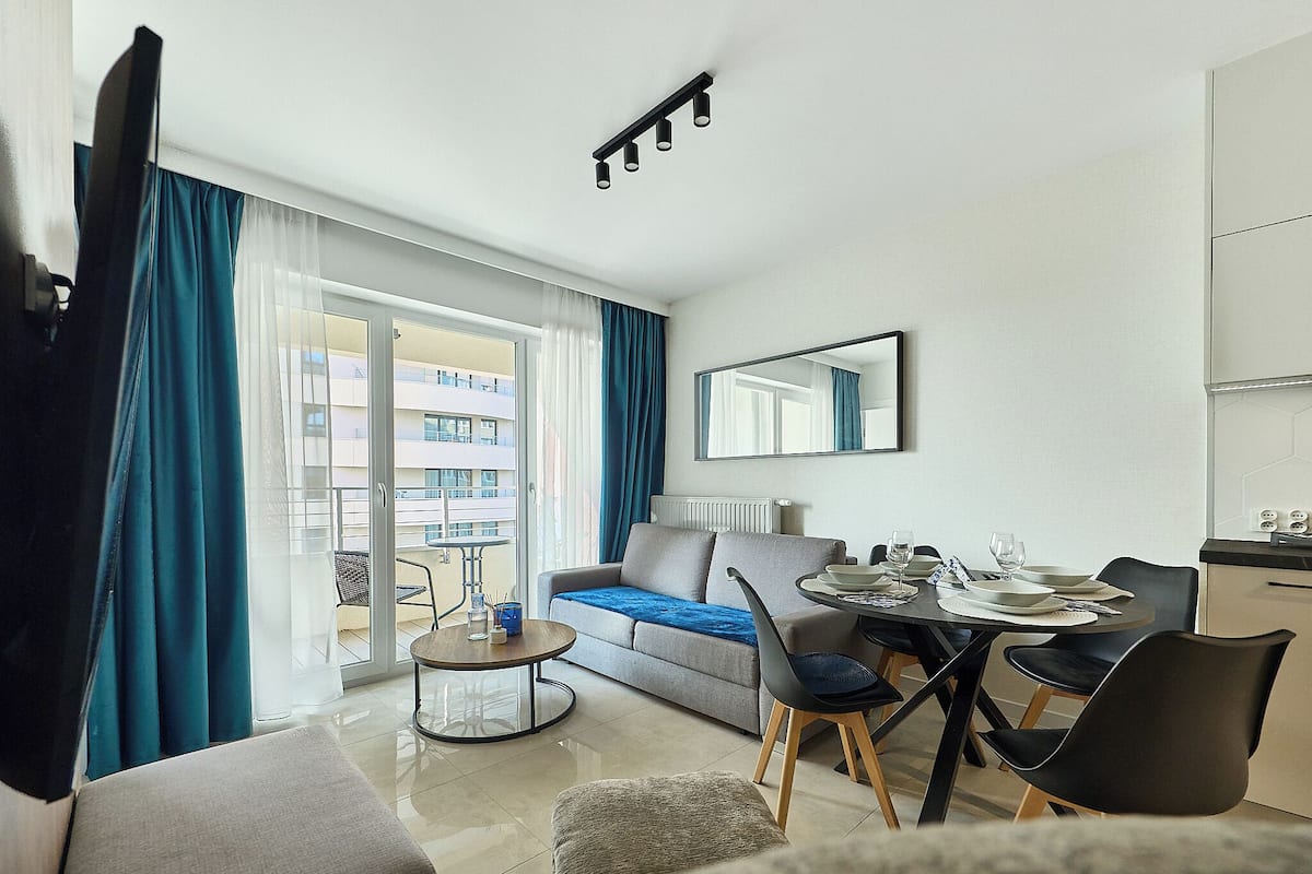 A modern living room with a sofa, dining table, chairs, and a large window with curtains.
