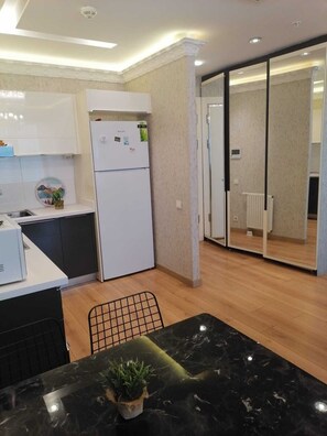 A modern kitchen with white cabinets, a built-in refrigerator, a dining table with a black marble top, and a potted plant. - Mall Of İstanbul Residence (Istanbul)