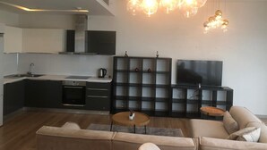 A modern kitchen with a built-in oven, a dining area with a sofa and a coffee table, and a TV mounted on the wall. - Mall Of İstanbul Residence (Istanbul)