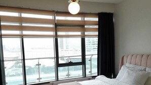 A modern bedroom with a large bed, a view of the city through floor-to-ceiling windows, and a pendant light. - Mall Of İstanbul Residence (Istanbul)