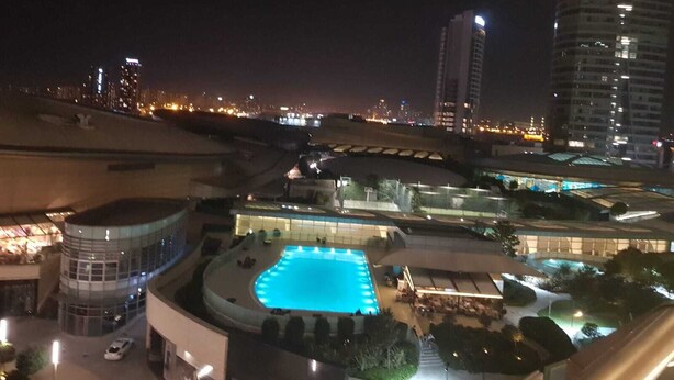 A hotel with a swimming pool, surrounded by modern buildings and a cityscape at night. - Mall Of İstanbul Residence (Istanbul)