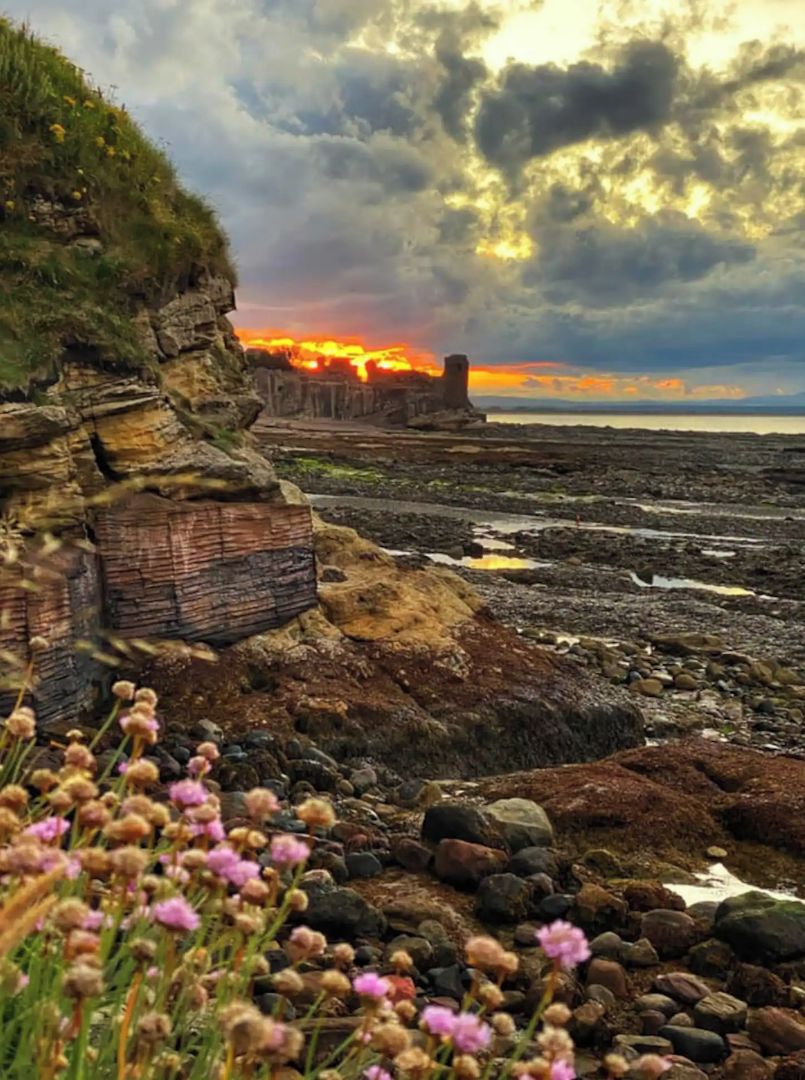 A coastal landscape with a rocky shoreline, a cliff, and a sunset in the background.