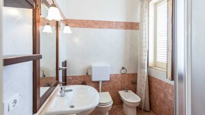 Une salle de bain équipée d’un lavabo, de toilettes, d’un bidet et d’une fenêtre avec des rideaux.