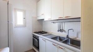 Une cuisine de taille réduite avec des meubles blancs, une cuisinière à gaz, un évier et une fenêtre.