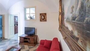 Un salon avec un canapé rouge, un téléviseur posé sur un meuble en bois, un tableau encadré et une fenêtre donnant sur l’extérieur.