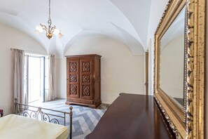 Quarto com cama, cômoda, espelho e lustre.