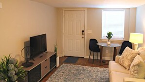 A living room with a TV, a dining table with chairs, a sofa, and a small plant by the window. - Red Bank Cozy Nest! (Chattanooga)