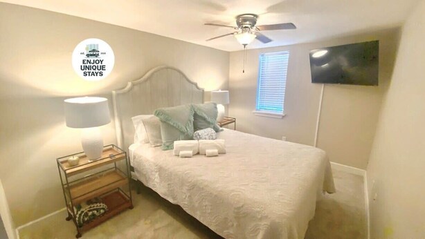 A bedroom with a bed, nightstands, a ceiling fan, a TV, and a window with blinds. - Red Bank Cozy Nest! (Chattanooga)