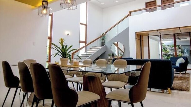 Un intérieur moderne avec une table à manger en verre, des chaises marron, un escalier et un canapé bleu.