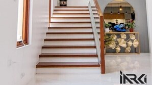 Un escalier moderne avec des marches en bois et une rampe en verre, menant à un espace repas d’où l’on a vue sur la cuisine.