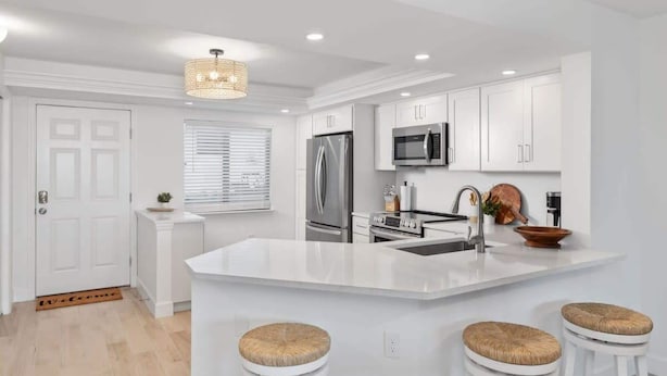 A modern kitchen with white cabinetry, stainless steel appliances, a central island with stools, and a chandelier. - Loggerhead 351 | Sunny Sanibel | Gorgeous Walkout Unit | Gulf Views (Sanibel)