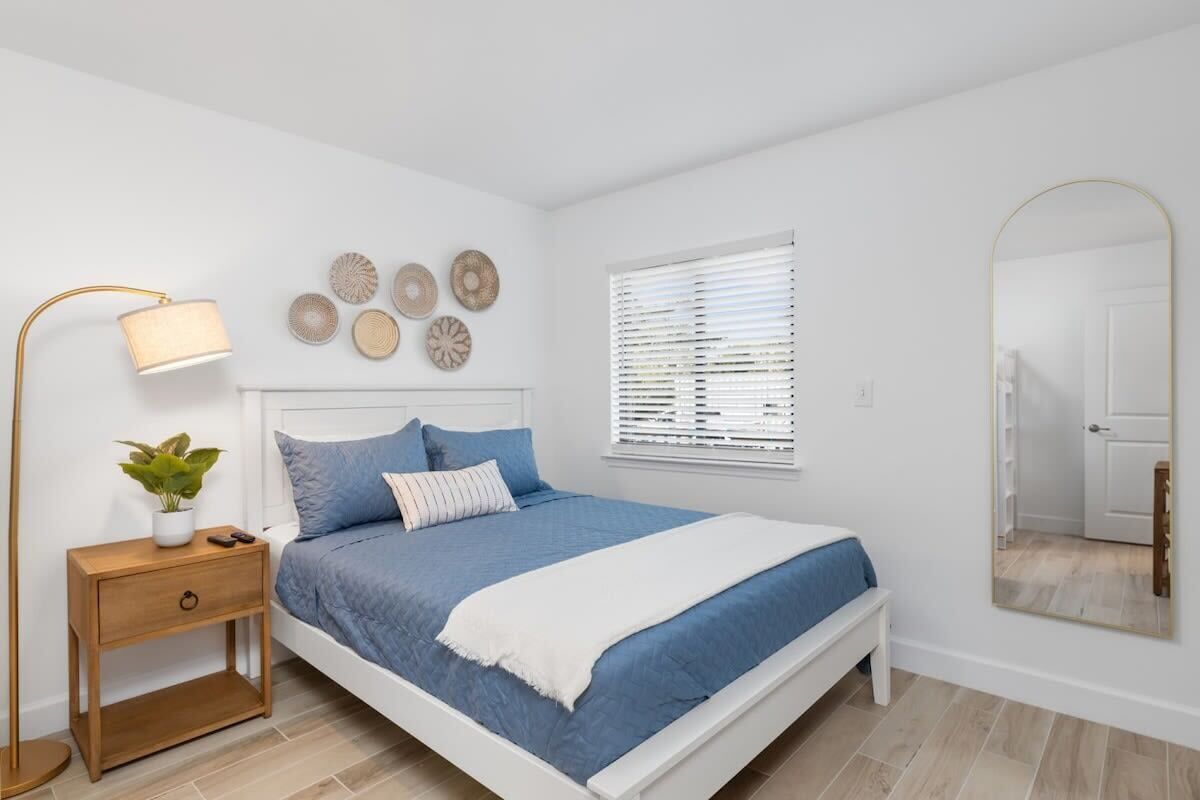 Un dormitorio con cama, mesita de noche, lámpara, decoración en la pared, ventana y espejo.