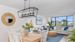 A modern living room with a dining area, a large window with a view, and a chandelier. - Loggerhead 351 | Sunny Sanibel | Gorgeous Walkout Unit | Gulf Views (Sanibel)