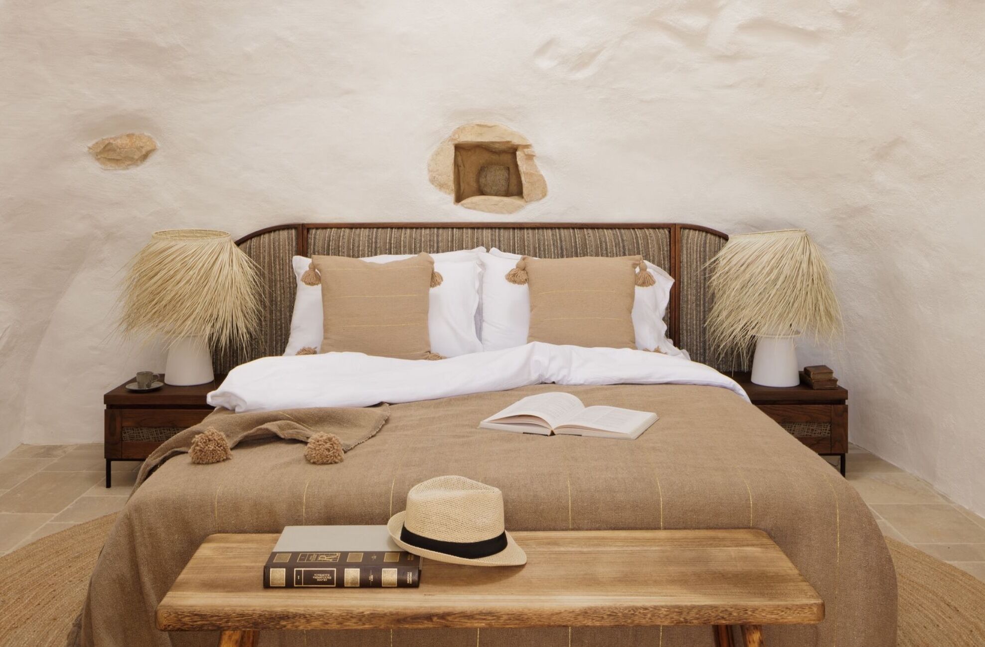 A bedroom with a bed, two bedside tables, a nightstand, a hat, and books.