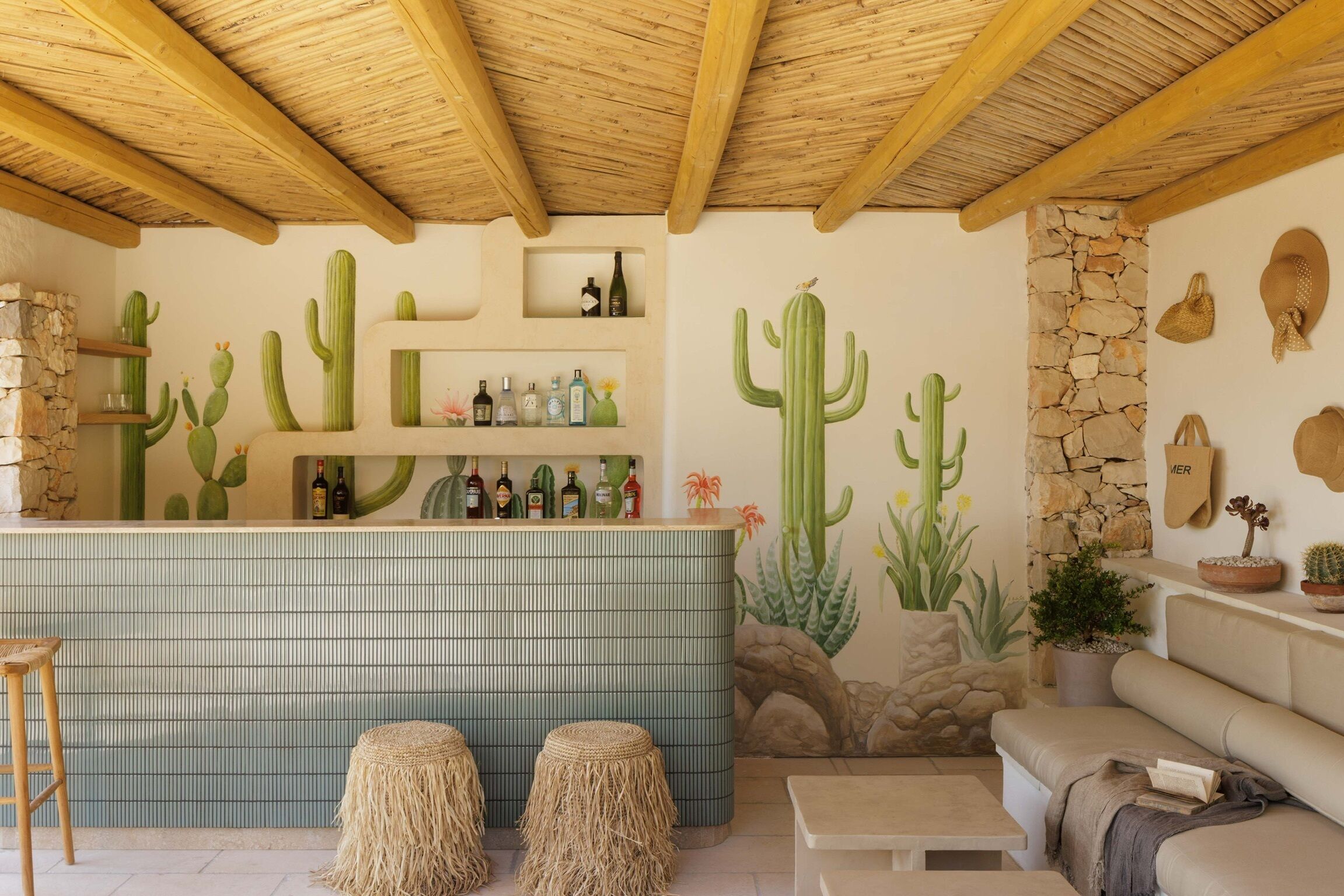 Un espace bar agrémenté d’une fresque représentant des cactus, de poutres en bois et d’un mur en pierre.