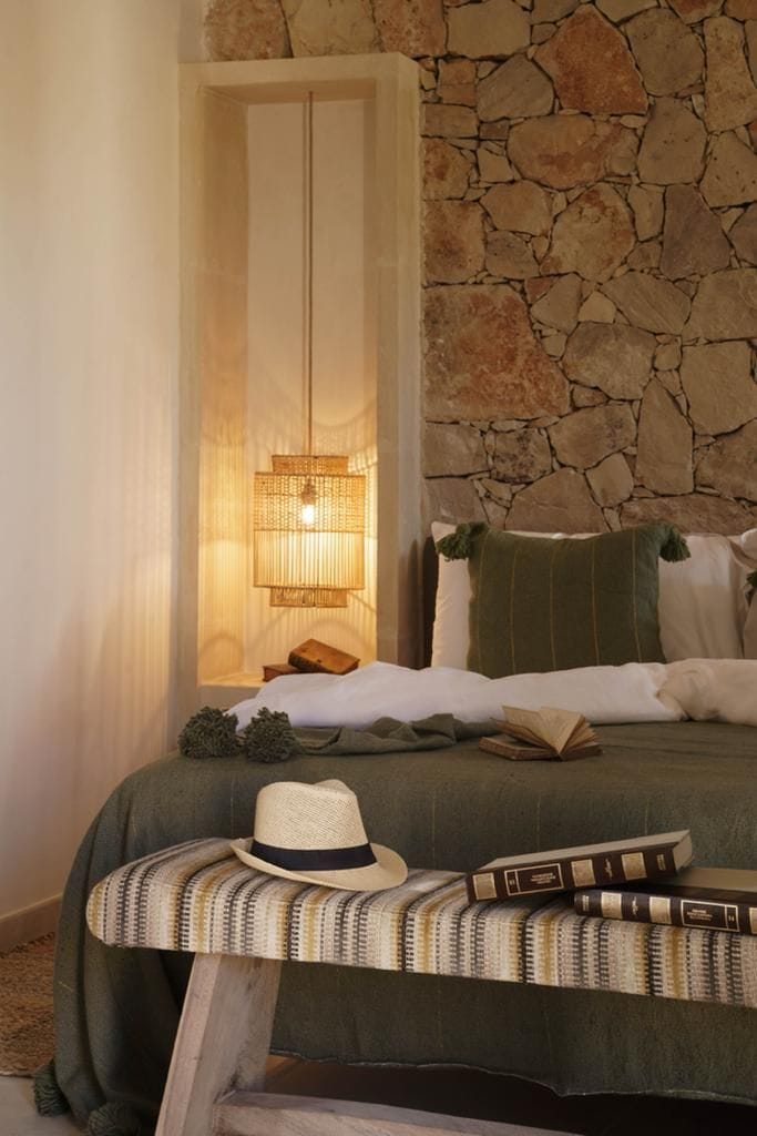 Un lit recouvert d’une couverture verte, un chapeau et des livres sur une table de chevet.