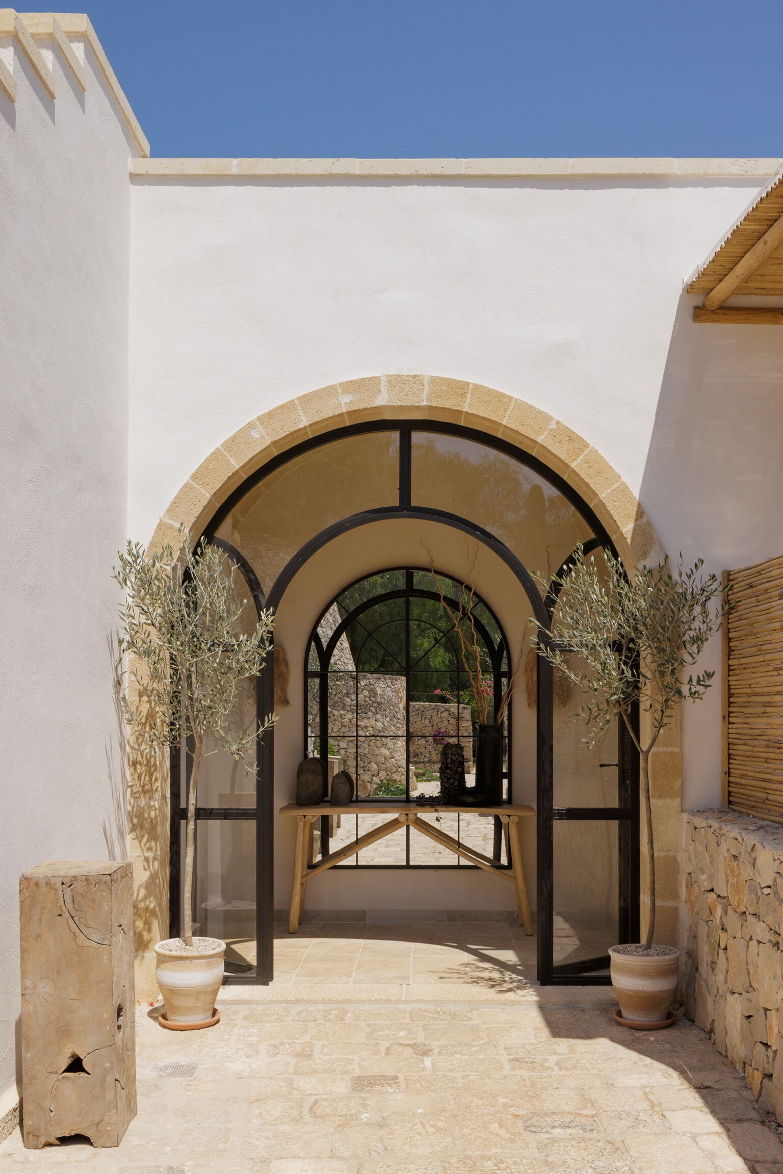 Un ingresso ad arco con piante in vaso, una panchina di legno e un muro in pietra.
