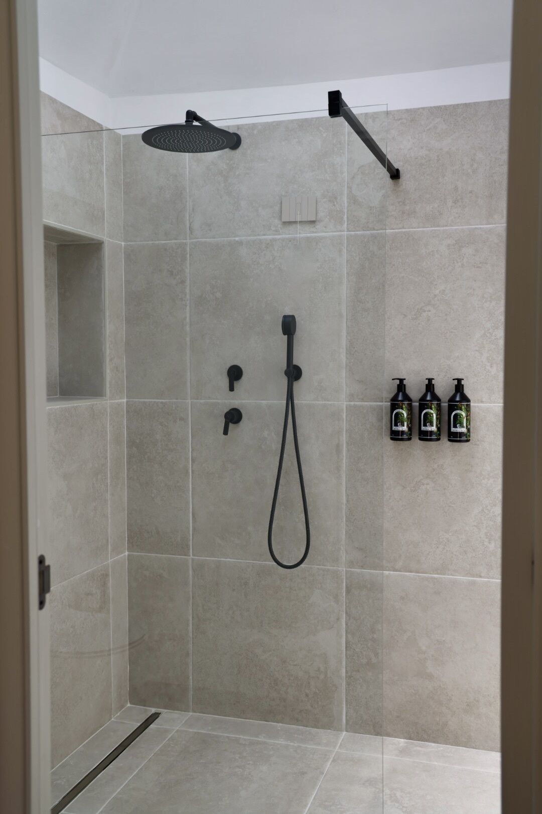 Een inloopdouche met een handdouche, een wanddouche en drie flessen shampoo.