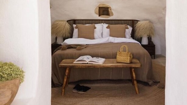 Un dormitorio acogedor con una pared de piedra rústica, una cama de madera, una mesita de noche con lámpara y una cesta tejida.