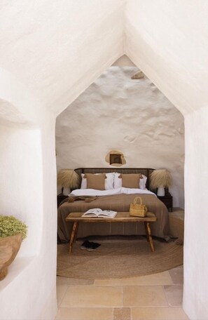 Un dormitorio acogedor con una pared de piedra rústica, una cama de madera, una mesita de noche con lámpara y una cesta tejida.