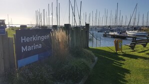Un port de plaisance où sont amarrés de nombreux bateaux, une pancarte indiquant « Port de Herkingen » et une table de pique-nique.