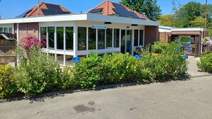 Un bâtiment à l’extérieur blanc et au toit recouvert de tuiles rouges, doté de grandes fenêtres et d’un espace d’entrée abrité.